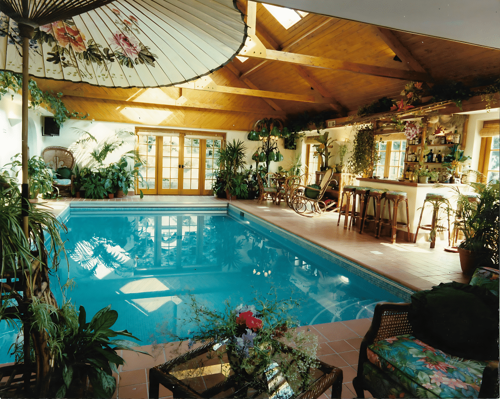 Indoor pool with plants, wooden ceiling, bar area, and lounge chairs.