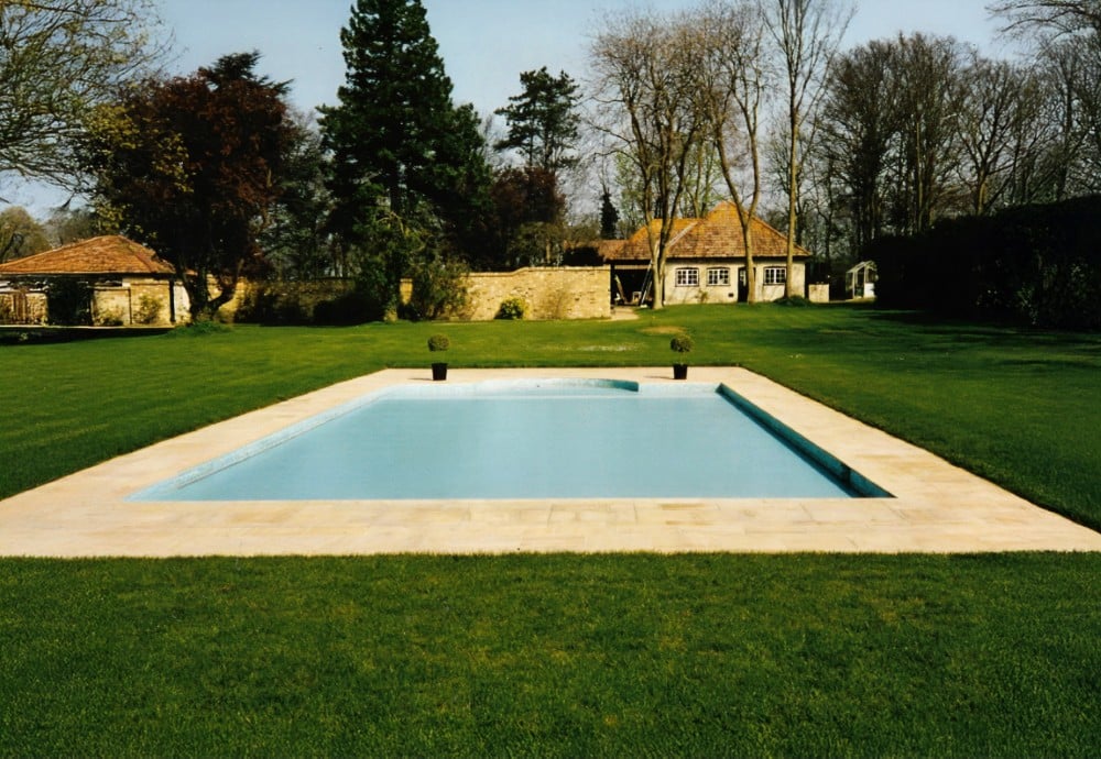 A rectangular outdoor swimming pool surrounded by grass and trees in a large garden.
