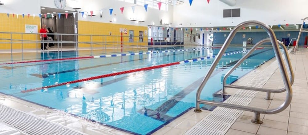 Indoor swimming pool with lane dividers, steps, and tiled floor at a leisure center.