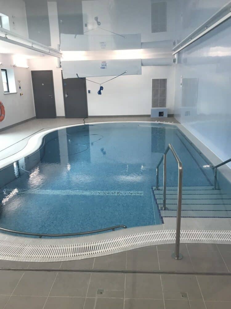 Small indoor pool with tiled steps, metal handrails, and surrounding white and grey tiles.